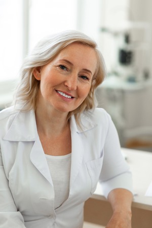 Leaning on the table. Pleasant blonde lady being experienced doctor and wearing representing robe during her shiftの写真素材