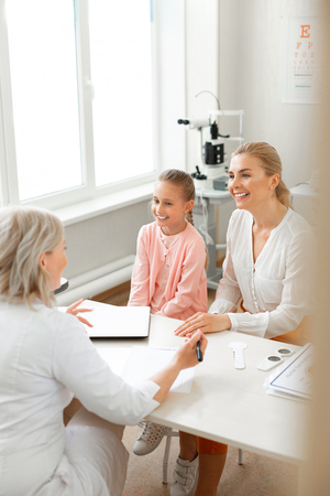Girl being comfortable. Smiling little child and pleasant mother sitting in front of experienced doctor and pleasantly talkingの写真素材