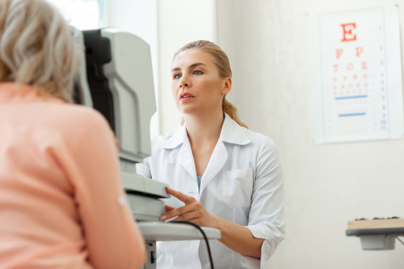 Deciding on recommendations. Professional skilled ophthalmologist being focused on visual inspection of eyes state during appointmentの写真素材