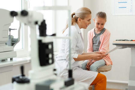 Observing construction. Caring pleasant doctor in white robe showing interesting picture to little calm patientの写真素材