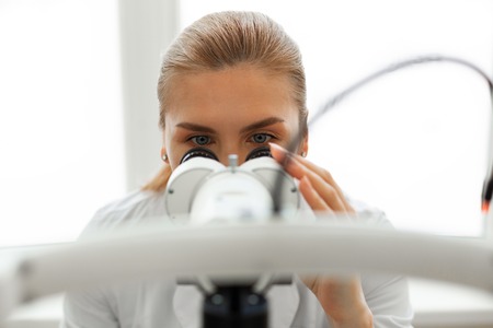Bright room. Serious busy oculist looking in binocular during investigation with complicated device