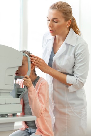Special device. Gentle serious ophthalmologist correcting position of her young patient during complicated sessionの写真素材