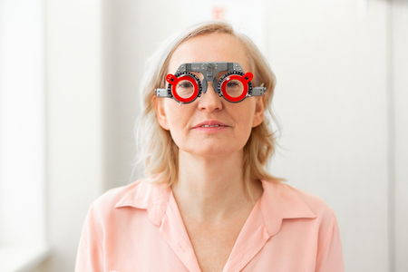 Control trying on. Calm senior patient in pink shirt having special construction on while trying on different lensesの写真素材