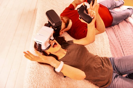 Funny moments. Smiling excited couple laying on the bed while playing a virtual gameの写真素材