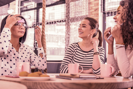Spotted blouse. Beautiful dark-haired woman wearing glasses and spotted blouse explaining word for her friendsの写真素材