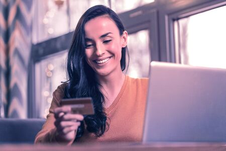 Successful payment. Delighted positive woman sitting near the laptop while looking at her credit...