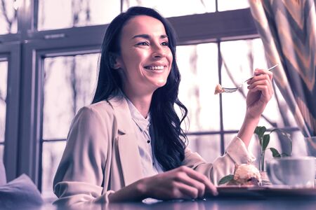 Wonderful taste. Delighted beautiful woman enjoying her tasty dessert while being in the cafeteriaの写真素材