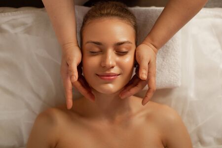 Improving skin state. Beaming flawless woman with gentle face showing pleasant smile while master touching her faceの写真素材
