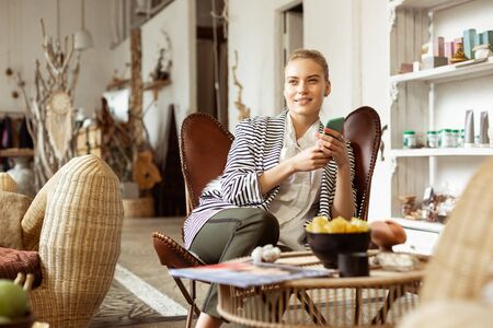 Carrying smartphone. Beaming good-looking woman in elegant outfit lying in leather armchair and...