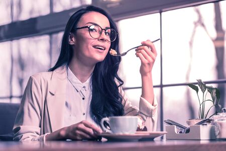 Very tasty. Pleasant attractive woman smiling while eating a delicious cake