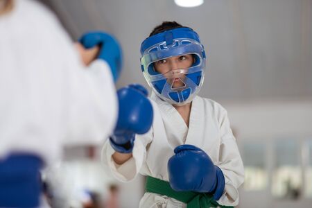 Boxing with friend. Active schoolboy wearing protective helmet and gloves boxing with friend