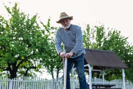 Having some rest. Retired grey-haired man having some rest while holding spade after digging groundの写真素材