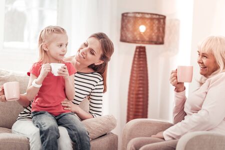 Tea time. Beautiful long-haired mother feeling gorgeous with her daughter while having tea together.
