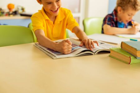 Joyful kid. Selective focus of boys hand on the book while sitting in the classroom
