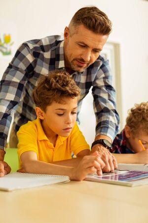 Helpful teacher. Smart bearded man helping his student while conducting a lesson