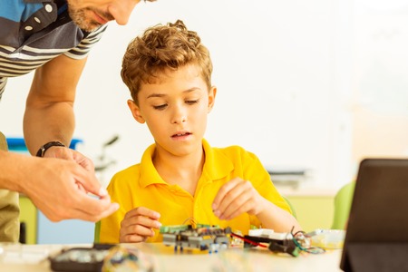 Modern education. Intelligent smart boy sitting in the classroom while constructing a robot