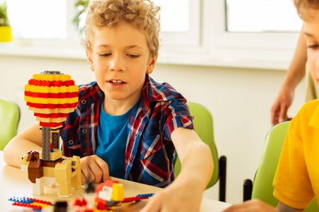 Constructing toys. Cute blonde boy taking some details from the constructor set while constructing...