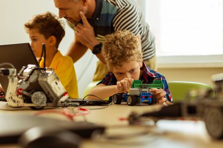Favourite hobby. Nice young boy sitting at the desk while playing with a car that he constructedの写真素材