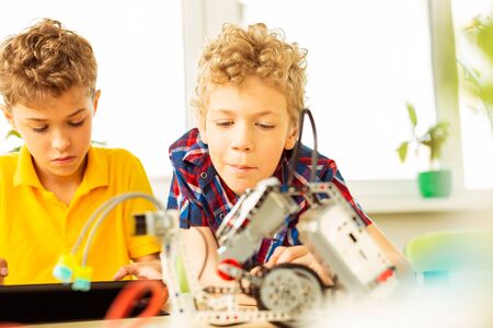 Lesson on robotics. Nice intelligent boys looking at the robot while having a science class on roboticsの写真素材