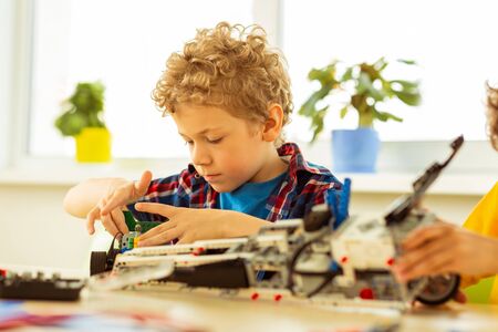 Being focused. Cute blonde boy concentrating on his task while constructing a car model