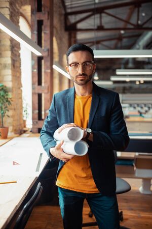 Experienced designer. Experienced interior designer standing in spacious office holding sketchesの写真素材