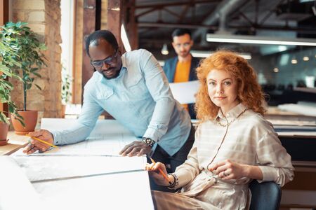 Sitting near boss. Blue-eyed appealing interior designer sitting near boss while working together