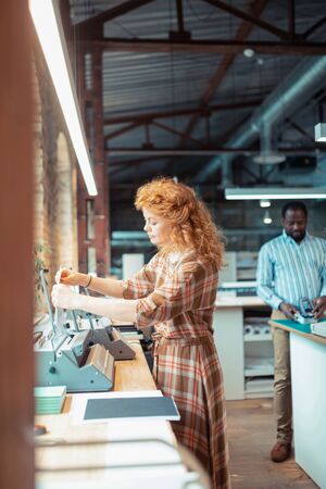 Wearing stylish dress. Curly red-haired beautiful woman wearing stylish dress using printer
