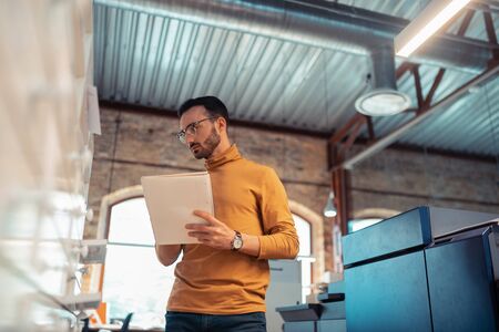 Man with notebook. Low angle of handsome bearded man wearing jeans orange polo neck holding notebook