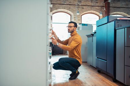 Dark-haired man. Handsome dark-haired man wearing black sneakers opening box in the printing office