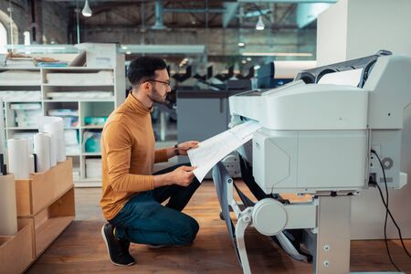 Man waiting. Dark-haired mature man waiting while printing paper with sketchesの写真素材