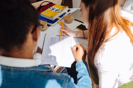 Need to check. Concentrated longhaired girl sitting near her friend and looking at answer chart