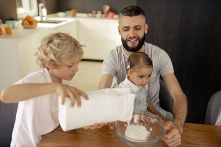 Young helper. Nice blonde boy holding a pack with flour while helping to cook breakfast