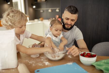 Helpful children. Nice cute small children putting hands in the flour while helping their father...