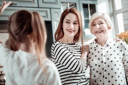 Funny girl. Cheerful young woman kindly looking at the emotional girl telling a story while standing next to her aged motherの写真素材