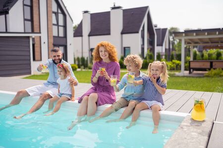 Near the water. Positive happy family sitting near the pool while putting their legs in waterの写真素材