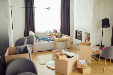 Dads love. Positive brunette man hugging his son while sitting with him on the sofaの写真素材