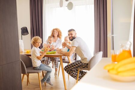 Ideal family. Happy delighted family looking at you while sitting together around the table in the dining roomの写真素材