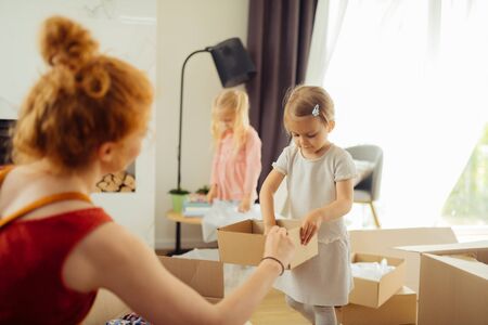 Young helper. Cute pretty girl looking into the box while helping her mother