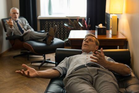 Tense man. Tense Caucasian male patient lying on the couch in front of his psychotherapist while...