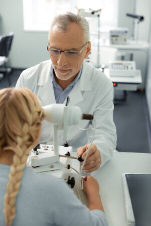 Doctor and girl. Blonde-haired girl with two braids visiting eye doctor feeling good