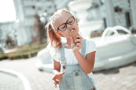 Sweet tooth. Concentrated little girl enjoying her ice-cream cone eating it closing her eyes in the summer.の写真素材