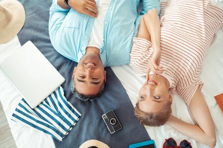 Great mood. Happy couple laying on the bed with all their stuff dreaming about their summer holiday together.の写真素材