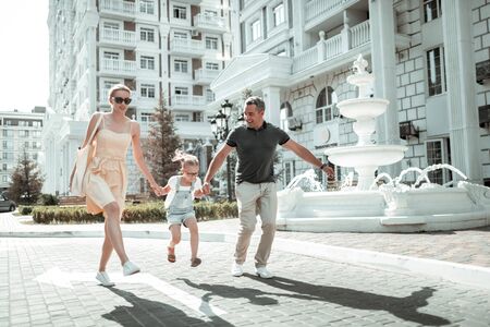 Having fun. Happy nuclear family holding hands skipping together along the street with the beautiful architecture.の写真素材