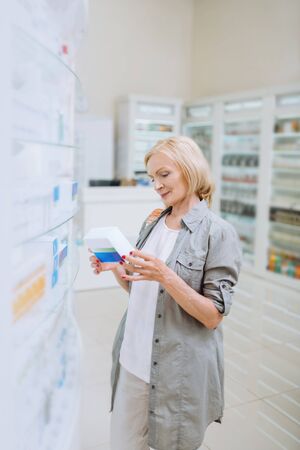 Mature client. Charming aged female keeping smile on her face while choosing medicineの写真素材