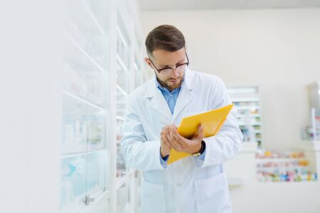 Sterile workplace. Competent chemist wearing glasses while working with documentsの写真素材