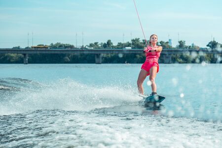 Perfect weekend. Modern young good-looking woman in stylish bright sportswear looking ahead while wakeboardingの写真素材