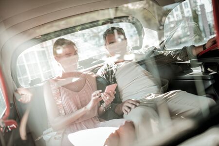 Laying the route. Cheerful husband and wife sitting together on the back seat of the car looking at...