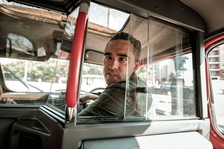 Having fun at work. Easy-going car driver grimacing turning back to his passenger on the backseat.