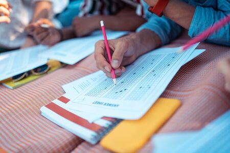 Preparing for exams. Hands of groupmates holding pencils training passing their tests lying on the blanket together.の写真素材