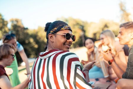 Genial company. Smiling boy wearing sunglasses spending evening having picnic with his university...